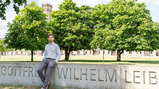 Ein Mann sitzt auf einer Steinmauer auf der die Buchstaben "Gottfried Wilhelm Leib" stehen.
